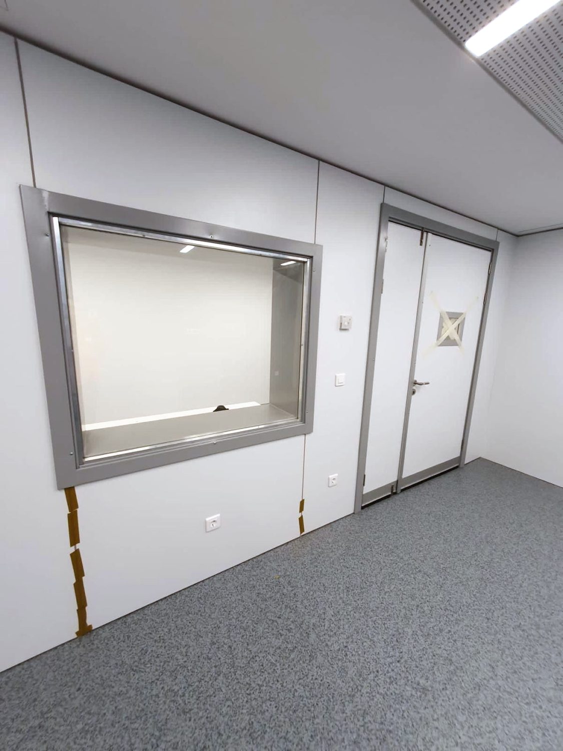 Sichtfenster aus Bleiglas neben einer zweiflügeligen Strahlenschutztür in derselben Wand